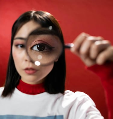 fekete hajú lány a nagyítón keresztül néz a kamerába