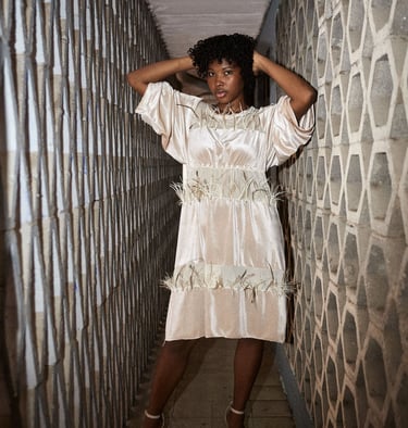 A stylish woman in a satin dress with feather trim poses in a narrow geometric stone hallway.