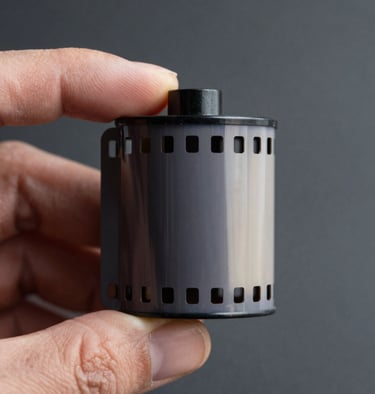 Macro shot of a vintage 35mm film strip held by a hand in an Angolana studio, moody lighting, featuring dark slate grey and off-white textures.