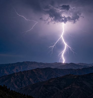A wide-angle photography shot of multiple lightning bolts spidering across a dark steel blue sky over a mountain range, International / Western.