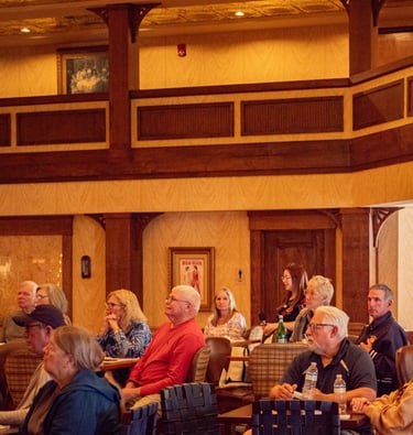 Audience seated in a warmly lit conference room, attentively listening to a presentation or speaker.