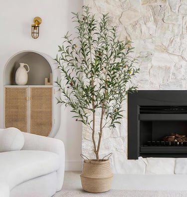 Tall artificial olive tree in a woven basket standing next to a modern fireplace and stone wall.