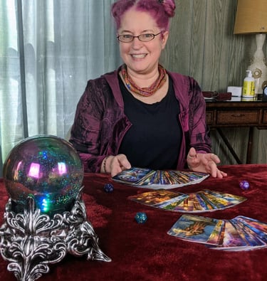 Renee with colorful tarot cards on a rich burgundy table cover, with deep blue crystal ball.