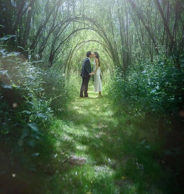 Newlywed couple sharing a kiss under a natural green willow archway in a sunlit garden forest.