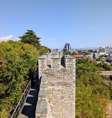 Historic stone walls of Skopje Fortress overlooking the modern city skyline and green trees in North Macedonia.