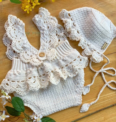 Handmade cream crochet baby romper with ruffled collar and matching sun hat on a wooden background.