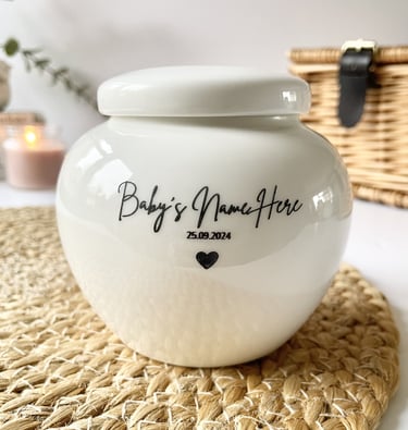 Rounded white ceramic urn with glossy finish, black script text “Baby’s Name Here 25.09.2024” and a 