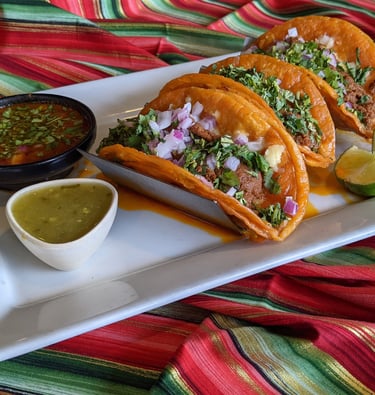 Plate of authentic Mexican beef birria tacos with cilantro, onions, lime, and dipping consomme.
