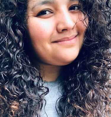 Smiling woman with long dark curly hair and natural makeup in a close-up portrait.
