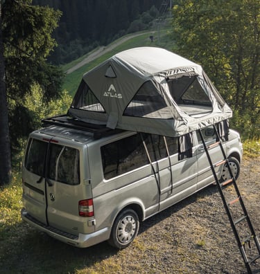 Atlas roof top tent mounted on a silver Volkswagen camper van parked in a scenic mountain forest.