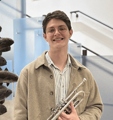 Jacob West in a jacket and glasses holding a trumpet