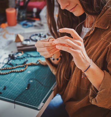 mujer elaborando joyeria con hilo de macrame y cuentas de piedras minerales en escritorio con mesa de corte
