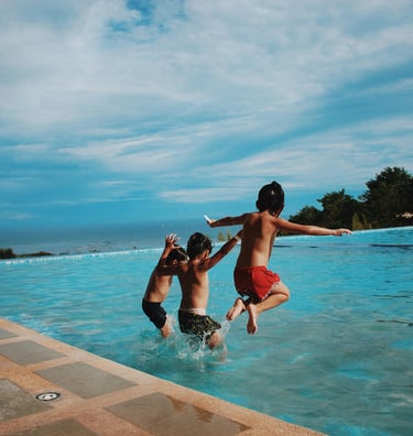 3 kids jumping into a pool. Text reads "family vacays." Linking to a page o family vacation ideas.
