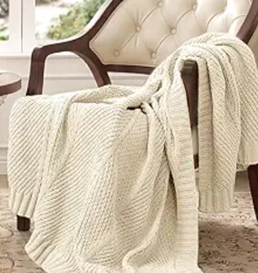 Cream cable knit throw blanket draped over a vintage tufted armchair.