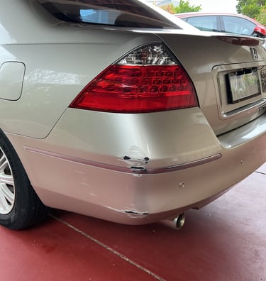 Rear bumper damage with paint scuffs and scratches on a silver sedan parked on a red driveway.