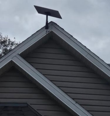 A Starlink satellite internet dish mounted on the peak of a residential roof against a cloudy sky.
