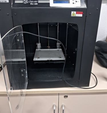 A black Cliever CL2 edu 3D printer with an open clear door sits on a white storage cabinet.