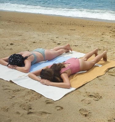 two women laying on a towel on a beach