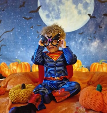 Young curly haired boy dressed as superman with a night backdrop for halloween special class.