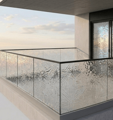 Modern high-rise balcony featuring decorative textured glass railings and an ocean view at sunset.
