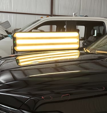 Professional PDR light board reflecting on a black car hood for paintless dent repair service.