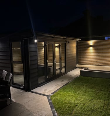 Modern garden room at night with outdoor lighting, patio, and lawn, creating an inviting backyard oasis.