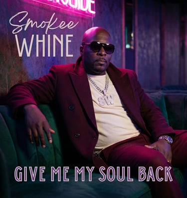 a man named Smokee Whine in a suit and sunglasses sitting on a couch