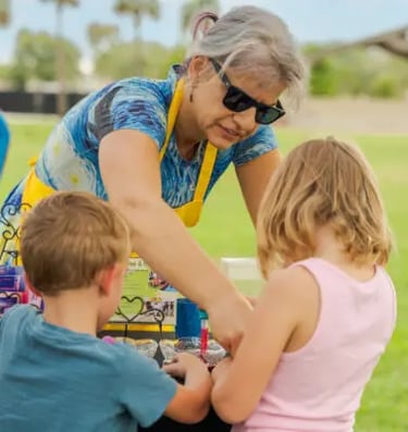 older woman helping two children with arts and craft activities