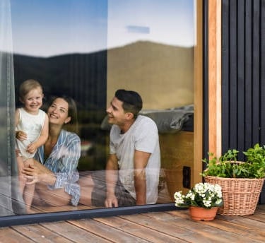 Una niña y sus padres están sentados en la ventana, todos están sonriendo.