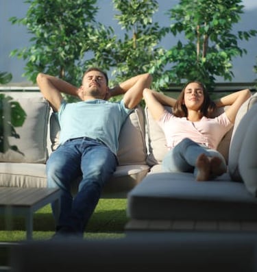 Una pareja tomando el sol en el sofá, con los brazos entrelazados detrás de la cabeza.