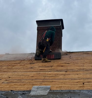 A roofing contractor repairs a brick chimney on a house during a residential roof replacement.