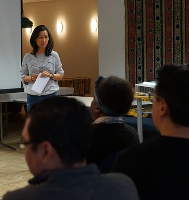 A professional woman presenting to a diverse audience during a business workshop or seminar.