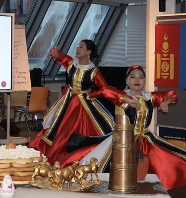 Mongolian dancers in traditional red deel costumes performing at a cultural event with folk decor.