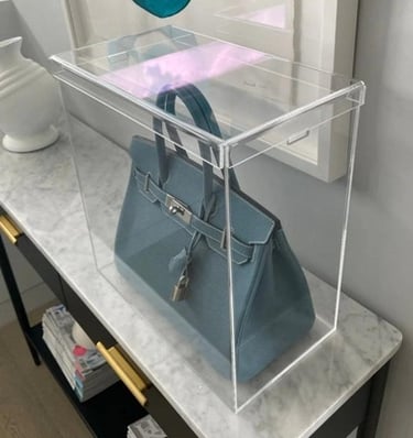 Clear acrylic display case showcasing a blue handbag on a marble table.