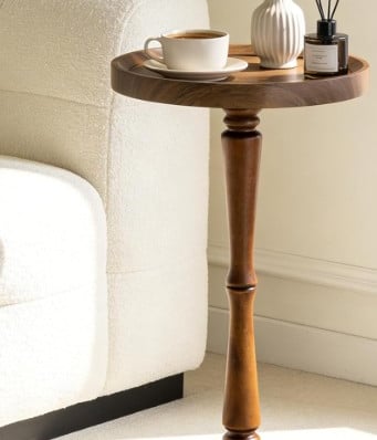 Round dark wood pedestal drink table or accent side table next to a white sofa.
