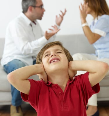 a young boy is holding his ears as a man is sitting on a couch with a woman holding her hands up. 