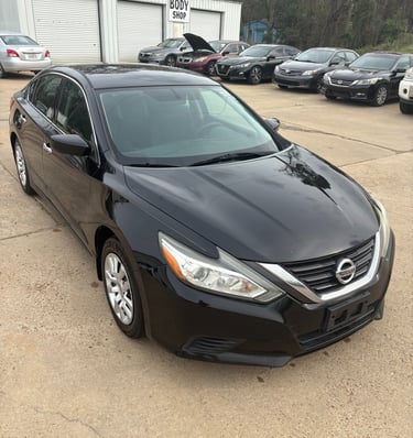 Black Nissan Altima sedan parked at an auto body shop and car repair lot.