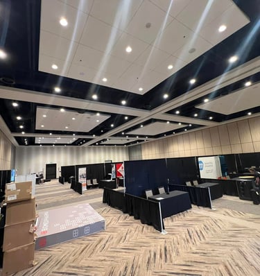 Empty convention hall setup with black booth curtains, professional lighting, and event signage.
