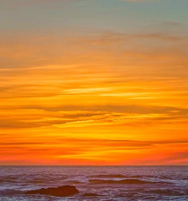 Vibrant orange sunset sky over ocean waves with a rocky beach shoreline at dusk.
