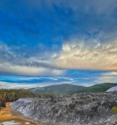 Scenic mountain landscape featuring a rocky talus slope and pine forest under a dramatic cloudy sky.