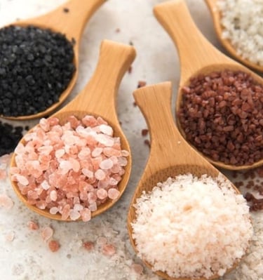 Wooden spoons filled with different salts: black, pink, white, red, salt on a light surface