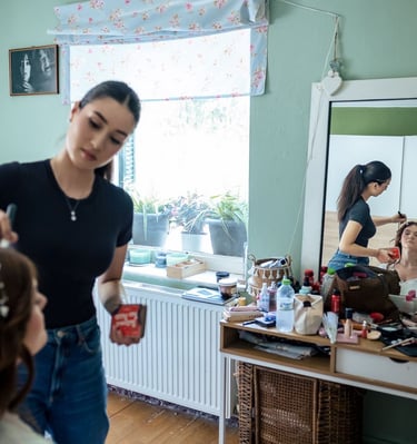 Bride sitting at vanity while makeup artist adds finishing touches — elegant bridal photo prep