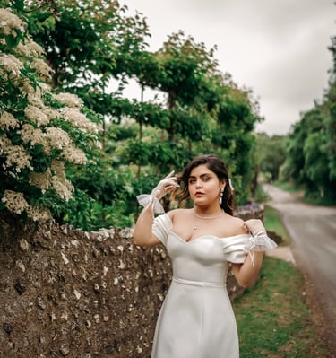 Bride in white dress posing by a stone wall with lush greenery, photographed in Kent.