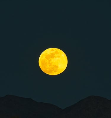 A glowing golden full moon shining brightly in a dark night sky above silhouetted mountain peaks.