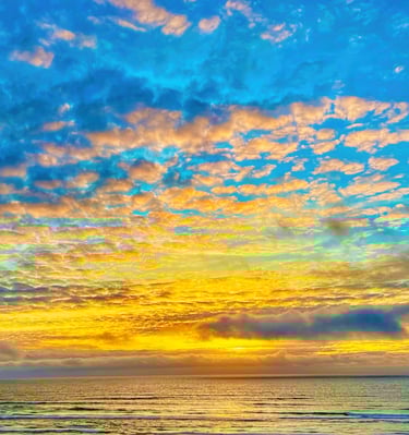 Vibrant ocean sunset with golden light reflecting on waves under a blue sky with fluffy altocumulus clouds.