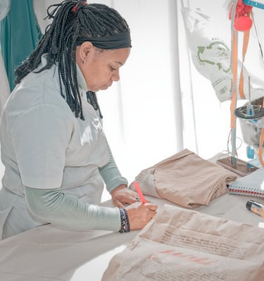 Modista trabajando en un taller de costura, marcando una prenda doblada sobre la mesa junto a una má