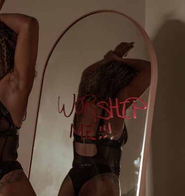 women in black lingerie hands resting on head in background worship me!! is written on mirror in red