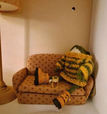 a couch with a sitting small knitted frog holding a pint of beer