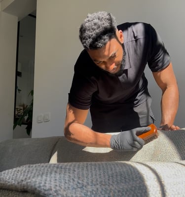 a man in a black shirt and gloves is cleaning a couch