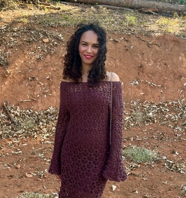 a woman in a brown crochet dress standing in front of a wooded area